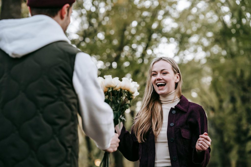 Loving boyfriend giving bouquet of flowers as present to happy girlfriend with long hair in park